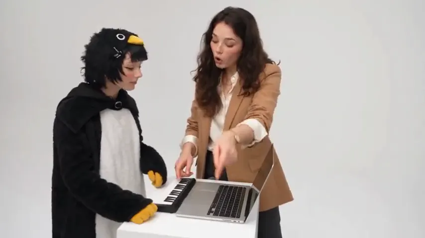 An Alors on Danse AI trend video: a person in a penguin onesie plays a mini keyboard, a friend in a tan blazer leans into the camera, then both walk off dancing in a white studio