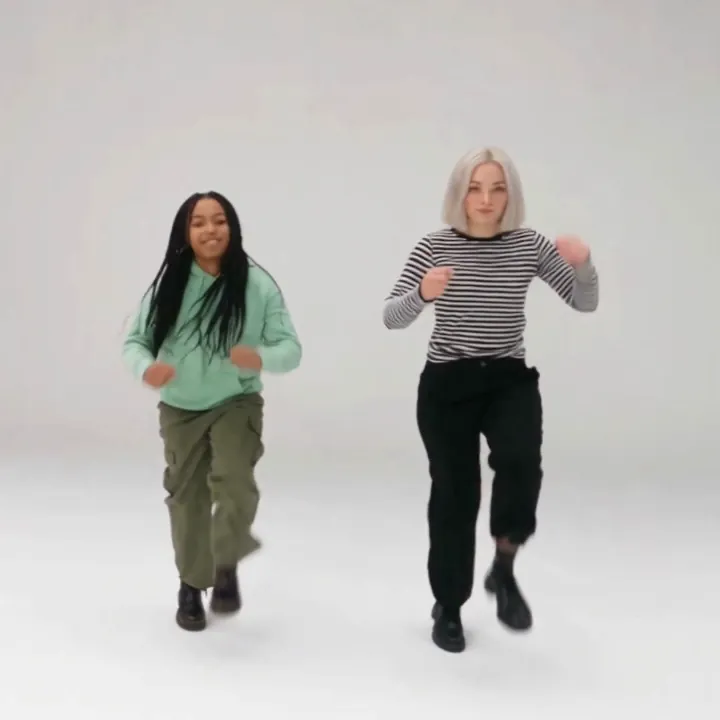 Two friends, one in a mint hoodie and one in a striped top, dance toward the camera across a white studio