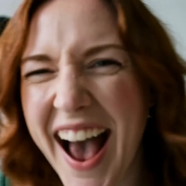 The close-up beat: the red-haired woman laughs right into the camera so her face fills the frame